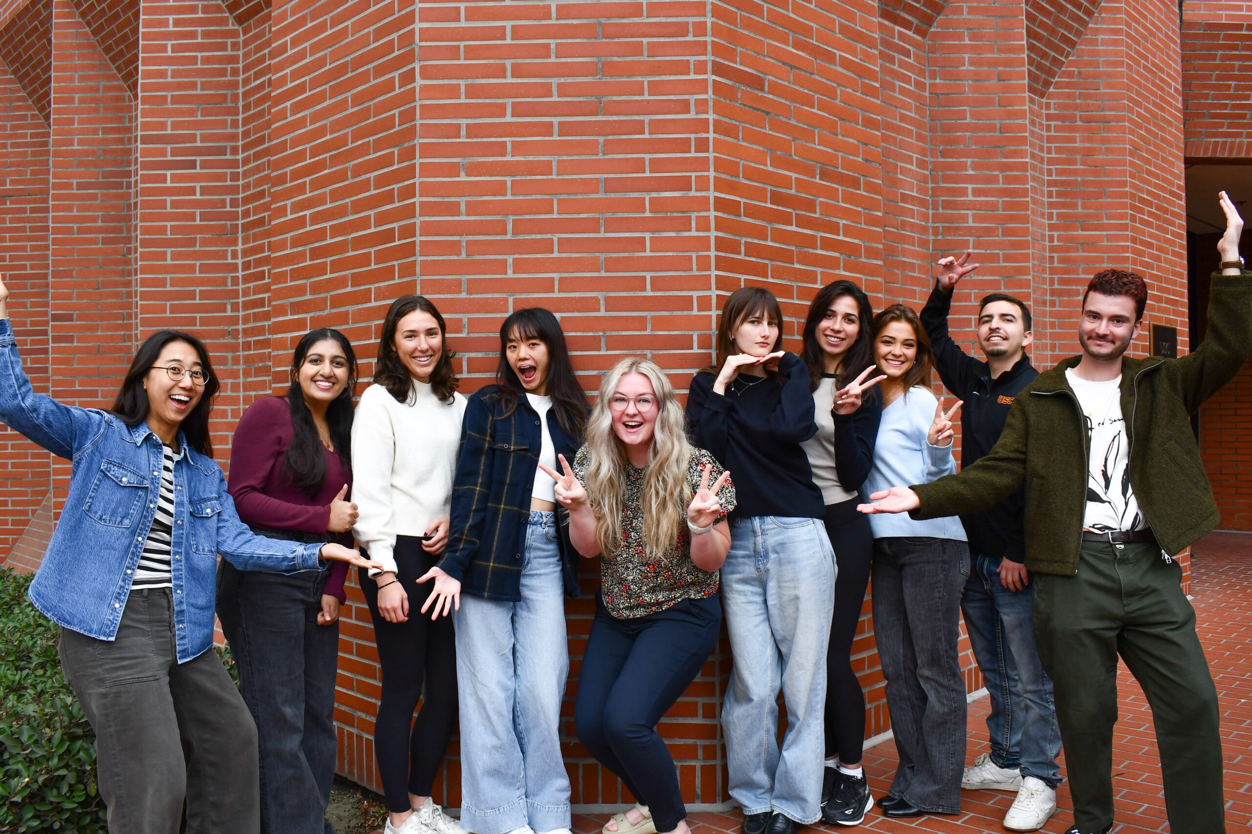 The 2024–2025 NGF Executive Committee, a diverse group of ten graduate students, stands in front of a brick building smiling and posing playfully for the camera.